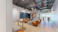 Located at 3169 Northwest Blvd in Upper Arlington, Ohio, this contemporary fitness facility offers a well-appointed, single-floor layout designed to support a full range of workout and wellness activities. The industrial-modern aesthetic is evident throughout, with exposed ductwork, open ceilings, and track lighting lending an energetic urban character to the space.

The main exercise room is generously sized, featuring patterned modular carpet tiles in yellow, gray, and tan tones. It is equipped with cardio machines including rowing machines, a stair climber, and cycling bikes positioned near large arched windows that invite natural light and outdoor views. A power rack with weight storage, a dumbbell rack, and a wall-mounted display screen round out the strength training area.

A dedicated group fitness studio features bold dark patterned wallcovering, mirrored walls, ceiling-mounted speakers, a wall-mounted TV, and open floor space ideal for classes or flexible training — finished with a pair of orange ottomans for versatile use.

The lounge area provides a welcoming transition space, furnished with warm cognac leather and upholstered seating, brass accent tables, light hardwood flooring, and a sculptural sputnik chandelier. Vibrant artwork and accent walls add personality throughout. A counter area with cabinetry and a cafe-style seating nook with bar-height chairs complete the amenity-rich environment.