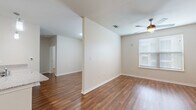 This single-floor residence is thoughtfully designed with a cohesive aesthetic that balances functionality and comfort throughout. Rich hardwood-style flooring flows through the main living areas, complemented by neutral walls and clean white baseboards that create a bright, inviting atmosphere.

The open-concept living and dining area is generously proportioned, with a ceiling fan providing airflow and a window fitted with blinds allowing natural light to filter in. A half-wall partition subtly defines the space while maintaining an open sightline toward additional rooms and the hallway beyond.

The kitchen is a functional highlight, featuring rich dark wood cabinetry, granite-style countertops, and a full suite of stainless steel appliances including a refrigerator, range, and microwave. Pendant lighting hangs above the extended peninsula, which also incorporates a sink — ideal for casual dining or meal preparation.

Bedrooms are carpeted for comfort, each equipped with a ceiling fan and window with blinds. One bedroom includes access to a walk-in closet with built-in shelving, offering practical storage.

The bathroom continues the cohesive design with dark wood cabinetry, a granite-style vanity top, and hardwood-style flooring, maintaining a consistent finish throughout the unit.