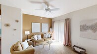 This thoughtfully designed single-floor residence offers a comfortable and cohesive layout with 1 bedroom and 1 bathroom. The living room serves as the heart of the home, featuring warm neutral-toned accent walls, plush carpeting, and a ceiling fan overhead. A sliding glass door floods the space with natural light, while the open layout connects seamlessly to both the dining and kitchen areas.

The kitchen is well-equipped with white cabinetry, dark countertops, white appliances including a refrigerator, electric range, and built-in microwave, all complemented by rich hardwood-style flooring. The adjacent dining area comfortably accommodates a round table and chairs, with a large decorative mirror enhancing the sense of space.

The bedroom is a serene retreat with soft carpet, a window dressed in sheer white curtains, and ample room to furnish comfortably. The bathroom features hardwood-style flooring, a shower with curtain, and clean white walls accented with decorative touches.

A welcoming entryway with carpeted flooring and bright white walls completes the unit. Throughout the space, warm neutral tones and consistent finishes create a cohesive, inviting ambiance ideal for comfortable everyday living.