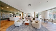 Located at 339 Boston Post Rd in Marlborough, MA, this single-floor amenity space spans a generous footprint and is thoughtfully designed to offer both social and wellness-focused environments. The open-concept lounge serves as the heart of the space, featuring warm hardwood flooring, plush curved seating in neutral tones, a central fireplace, wall-mounted TV, and floor-to-ceiling windows that flood the interior with abundant natural light and offer views of the surrounding landscape. A dedicated billiards area flows seamlessly from the lounge, centered around a handsome pool table and complemented by large windows overlooking lush outdoor scenery. Adjacent to this, a stylishly appointed bar and social area showcases deep green cabinetry, pendant lighting, bar seating, and decorative wall accents, creating an intimate yet vibrant atmosphere. The fitness center is divided into distinct zones: a cardio area with treadmills, ellipticals, and stationary bikes positioned beneath a drop ceiling with ample window views, and a strength training zone featuring free weights, benches, cable machines, and wall mirrors. A hallway connects the zones, with glass-panel doors providing visual transparency throughout. The overall design balances modern aesthetics with comfort, creating a welcoming, multi-functional communal destination.