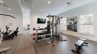 Located at 157 Hathaway Ln in Mooresville, NC, this fitness center offers a thoughtfully designed single-floor layout that divides its generous floor area into two distinct functional zones. The cardio area features a row of True-brand treadmills, elliptical trainers, and rowing machines arranged along bright white walls lined with multiple windows that flood the space with natural light. Ceiling fans overhead provide comfortable airflow during workouts, and wall-mounted flat-screen TVs keep users entertained. The flooring transitions from textured carpet in the cardio zone to durable rubber flooring in the strength training area, providing appropriate surfaces for each activity. The strength and free weights zone is outfitted with an Atlas multi-functional cable machine, a heavy punching bag, battle ropes, a full rack of dumbbells, and medicine balls, catering to a wide range of training styles. Floor-to-ceiling mirrors line the walls of the strength area, enhancing the sense of openness and allowing users to monitor their form. Recessed lighting throughout the facility ensures consistent, even illumination. The clean, white interior palette and open layout create a motivating and professional gym environment suitable for all fitness levels.