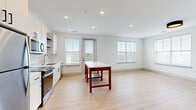 Located at 5025 Huntly Ridge St in Charlottesville, Virginia, this well-appointed three-bedroom, two-bathroom residence offers a thoughtfully designed single-floor layout with clean, modern aesthetics. The open-concept kitchen and living area serves as the heart of the home, featuring light wood-tone flooring, recessed lighting, and multiple windows that flood the space with natural light and provide pleasant neighborhood views. The kitchen is outfitted with white cabinetry, open wood shelving, a light-toned tile backsplash, stainless steel appliances including a range, microwave, and dishwasher, and a sleek undermount sink — all complemented by black hardware accents for a contemporary touch. The three bedrooms offer comfortable proportions, with the generously sized primary bedroom providing ample space. Two of the bedrooms feature plush carpeting and ceiling fans, while an additional bedroom showcases the same light wood flooring found throughout the main living areas. Each room benefits from natural light through window treatments. The two bathrooms are finished in crisp white with modern vanities, large mirrors, and brushed metal or gold-tone fixtures. One bathroom features a full tub-shower combo, while the other offers an elongated vanity layout. The overall ambiance is bright, clean, and move-in ready.