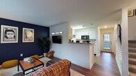 Located on Croyden Avenue in Kalamazoo, Michigan, this two-floor residence offers a well-organized layout designed for comfortable everyday living. The main level centers around an open-concept living and dining area distinguished by bold navy blue accent walls that create a striking visual contrast against the light grey surroundings and wood-look flooring that runs throughout. The living room provides generous space for seating and entertainment, with windows allowing natural light to filter in. Adjacent to it, a defined dining nook features the same navy accent wall and window with blinds, creating an intimate setting. The kitchen is positioned just off the living area, separated by a peninsula counter with granite-style surfaces. White cabinetry lines the walls alongside black appliances, including a refrigerator, range, and microwave, with ample counter and storage space. A full bathroom on the main level features wood-look flooring, a tub-shower combination, vanity with storage, and a large mirror. Upstairs, the bedrooms offer a quieter retreat, with carpeted floors, windows with natural light, and ceiling fixtures. A second full bathroom on this level mirrors the clean, functional design found throughout. The overall ambiance is modern and cohesive, with consistent design choices tying both floors together.