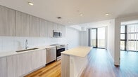 Located at 2800 SW 27th Terrace in Miami's vibrant Coconut Grove neighborhood, this modern 2-bedroom, 1-bathroom residence offers a thoughtfully designed layout with clean lines and a contemporary aesthetic throughout. The open-concept kitchen is a standout feature, showcasing floor-to-ceiling light wood cabinetry, white subway tile backsplash, a full suite of stainless steel appliances including a range, dishwasher, microwave, and refrigerator, and a generous white quartz island that flows seamlessly into the living area. Warm wood-style flooring runs throughout the entire residence, adding a welcoming contrast to the crisp white walls and recessed lighting overhead. The living area opens to a private balcony through floor-to-ceiling sliding glass doors, offering elevated views of the surrounding Miami cityscape. Both bedrooms are bright and airy, with large windows framing sweeping outdoor views and vertical blinds for privacy. The primary bedroom provides a comfortable footprint with generous natural light. The full bathroom is finished in a clean, minimalist style with a white tile tub-shower combo, stone-topped vanity with wood cabinetry, and large-format tile flooring. A dedicated closet completes the efficient and well-appointed floor plan.