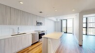 Located at 2800 SW 27th Terrace in Miami's vibrant Coconut Grove neighborhood, this modern 2-bedroom, 1-bathroom residence offers a thoughtfully designed layout with clean lines and a contemporary aesthetic throughout. The open-concept kitchen is a standout feature, showcasing floor-to-ceiling light wood cabinetry, white subway tile backsplash, a full suite of stainless steel appliances including a range, dishwasher, microwave, and refrigerator, and a generous white quartz island that flows seamlessly into the living area. Warm wood-style flooring runs throughout the entire residence, adding a welcoming contrast to the crisp white walls and recessed lighting overhead. The living area opens to a private balcony through floor-to-ceiling sliding glass doors, offering elevated views of the surrounding Miami cityscape. Both bedrooms are bright and airy, with large windows framing sweeping outdoor views and vertical blinds for privacy. The primary bedroom provides a comfortable footprint with generous natural light. The full bathroom is finished in a clean, minimalist style with a white tile tub-shower combo, stone-topped vanity with wood cabinetry, and large-format tile flooring. A dedicated closet completes the efficient and well-appointed floor plan.