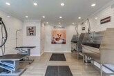 Located at 3400 Winterset Pkwy SE in Marietta, Georgia, this pet grooming facility is thoughtfully designed to provide a clean, functional, and welcoming environment for pets and their owners. The single-floor space is finished throughout with classic white subway tile walls, light wood-look tile flooring, and recessed lighting, creating a bright and hygienic atmosphere.

The facility is divided into two primary functional zones. The bathing area features multiple stainless steel grooming tubs equipped with professional-grade spray attachments, built-in steps for easy pet access, and white cabinetry for supply storage. Anti-fatigue rubber mats are positioned strategically for safety and comfort.

The grooming area is outfitted with adjustable height grooming tables and a wall-mounted professional dryer arm, allowing for efficient and thorough grooming sessions. Large black-framed windows flood this area with natural light and offer views of the surrounding greenery, creating an open and airy feel.

Throughout the space, playful pet-themed artwork and signage — including a charming "Pets Are" wall mural — add warmth and personality. The facility includes a secure entry door with keypad access, ensuring a controlled and safe environment. Overall, the space combines practical, professional-grade equipment with a clean and cheerful aesthetic.