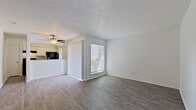 This single-floor residence offers a clean, functional layout designed for comfortable everyday living. The open living area is bright and welcoming, featuring durable wood-look flooring, neutral light gray walls, and a textured ceiling with a ceiling fan that provides both comfort and ventilation. Natural light flows in through windows fitted with horizontal blinds, creating an airy and pleasant atmosphere throughout. A half-wall partition separates the living space from the kitchen area, maintaining an open connection between the two.

The galley-style kitchen is well-equipped with white cabinetry, granite-look countertops, a subway tile backsplash, a stainless steel double sink, and black appliances including a refrigerator and electric range. A window above the kitchen area brings in additional natural light.

The unit includes two bedrooms, each with wood-look flooring, ceiling fans with lighting, and ample closet space. One bedroom features an open built-in closet with shelving, while the other offers a sliding-door closet. Both rooms are generously sized and filled with natural light from exterior windows.

The bathroom includes a full-size soaking tub with a shower combo, finished with clean white tile surround. A spacious secondary living or flex area near the entry provides additional versatile space. Throughout, the consistent flooring and neutral palette create a cohesive and move-in-ready environment.