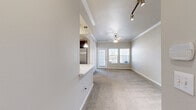 This single-story, one-bedroom, one-bathroom residence offers a thoughtfully designed open-concept layout that maximizes its comfortable footprint. The living room is finished with plush carpet, crown molding, and a ceiling fan, while track lighting adds a modern touch. A large glass door opens to an outdoor area, allowing natural light to fill the space. The kitchen is accessible via a pass-through peninsula with a white countertop, creating seamless connectivity to the living area. Inside, the kitchen features rich dark wood cabinetry, a classic white subway tile backsplash, light tile flooring, stainless steel appliances including a refrigerator, electric range, and built-in microwave, plus a full-sized pantry enclosed by double doors. The bedroom is generously sized, carpeted, and highlighted by a striking arched window that frames outdoor views, complemented by a ceiling fan. It connects directly to a spacious walk-in closet outfitted with multi-tiered wire shelving and hanging rods. The bathroom includes a dark wood vanity with a white countertop, tile flooring, and a glass-enclosed walk-in shower with tile surround, offering a clean, functional design throughout.