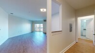 This single-floor residence offers a well-organized layout that balances open communal spaces with private living areas. The living room is a spacious, light-filled area anchored by wood-style laminate flooring and large sliding glass doors that lead to a private balcony, providing views of the surrounding brick exterior buildings and allowing natural light to fill the room. A thermostat and HVAC vent are conveniently positioned nearby, reflecting practical design throughout.

The kitchen is thoughtfully appointed with two-tone cabinetry—white upper cabinets and gray lower cabinets—complemented by granite-style countertops, a stainless steel refrigerator, gas range, microwave, and dishwasher. A matte black faucet over a single-basin sink adds a contemporary touch, and the space opens toward the main living area via a half-wall peninsula.

The bedrooms feature soft, neutral-toned carpet and ample wall space. One bedroom includes access to a walk-in closet and connects to a bathroom, while another benefits from a window with outdoor views. The bathroom includes a full soaking tub with white subway tile surround, accented by decorative mosaic tile borders, paired with white cabinetry and granite-style countertops.
