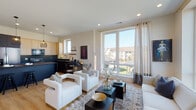 Located at 288 Stonington Dr in Bloomingdale, IL, this contemporary single-floor residence offers a thoughtfully designed open-concept layout with modern finishes throughout. The living area is a standout, bathed in natural light streaming through large floor-to-ceiling windows dressed with elegant draping curtains. The space comfortably accommodates generous seating arrangements and opens to views of the surrounding neighborhood. Light hardwood flooring flows seamlessly throughout, complementing the neutral color palette.

The kitchen is a sleek, design-forward space featuring light wood flat-front cabinetry, dramatic dark quartz countertops, a matching dark island with bar seating, and stainless steel appliances. Stylish pendant lighting adds warmth overhead, while an adjacent dining nook provides an intimate setting for meals.

The bedroom is a serene retreat, offering ample space, warm hardwood floors, and access to a private outdoor balcony through expansive glass doors framed by soft linen curtains. The bathroom features a clean, minimalist aesthetic with a soaking tub, wood-tone flooring, gray walls, and a tall narrow window that introduces soft natural light. This residence blends contemporary design with functional living in a well-appointed Bloomingdale community setting.
