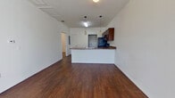 This single-story unit is designed with a practical, open layout that integrates the living and kitchen areas into one cohesive space. Rich, dark hardwood-style flooring runs throughout the main living areas, providing a warm contrast to the crisp white walls. The entry foyer receives natural light through a nearby window, creating a bright and welcoming first impression.

The kitchen is positioned at the heart of the unit and features a peninsula with a granite-style countertop, offering both workspace and a natural divider from the living area. Rich dark cabinetry lines the walls above, complemented by black appliances including a refrigerator, range, microwave, and dishwasher. Pendant lighting hangs above the peninsula, adding a focused, functional aesthetic. A walk-in pantry or storage closet is accessible directly from the kitchen.

The bedroom areas transition to neutral-toned carpet, contributing a softer feel. Bedrooms are generously proportioned, with large windows that allow ample natural light to fill the space. One bedroom features a ceiling fan and access to a private bathroom, while additional doors lead to closet space. The overall ambiance is clean, functional, and move-in ready.