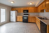 This two-story home offers a practical and functional layout spread across two levels, connected by a staircase visible in the floor plan. The kitchen is a standout space, featuring an L-shaped configuration with warm honey-oak cabinetry extending to the upper walls, providing generous storage throughout. Light-toned countertops offer ample prep space, and the kitchen is equipped with black appliances including a range, built-in microwave, dishwasher, and a white refrigerator. Neutral vinyl tile flooring completes the space.

The bedrooms are carpeted in neutral tones and each include a ceiling fan with integrated lighting and windows fitted with blinds that allow natural light. Closet access is available in the bedrooms, adding practical storage. The bathrooms are consistent in design, each featuring warm oak vanity cabinetry, a single-basin sink with light countertops, a tub-shower combination, an overhead cabinet for additional storage, and tile flooring. The overall aesthetic throughout the home is neutral and understated, with taupe and beige wall tones creating a calm, cohesive atmosphere across all rooms.