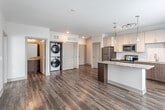 This single-floor residence at 1901 Locust St in Kansas City, Missouri offers a well-designed open-concept layout with contemporary finishes throughout. The kitchen serves as a central highlight, featuring crisp white upper cabinetry paired with rich dark wood lower cabinets, a decorative geometric tile backsplash, and granite-topped counters. A peninsula island with a granite surface provides additional prep space and casual seating, while pendant lights and a track lighting system illuminate the area. Stainless steel appliances, including a refrigerator, range, microwave, and dishwasher, complete the kitchen. Wood-style plank flooring extends through the main living and kitchen areas, adding warmth and visual continuity. The living area is generously proportioned, benefiting from multiple windows that invite natural light and offer access to an outdoor space. A bedroom features plush carpeting and neutral walls, providing a quiet retreat. The bathroom includes a full soaking tub with shower combination, chrome fixtures, and a safety grab bar. A dedicated in-unit laundry closet with stacked washer and dryer adds everyday convenience, while ample interior doors allow for versatile use of the available spaces.