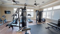 This dedicated fitness center is thoughtfully designed to support a comprehensive workout experience. The space features hardwood-style flooring paired with neutral-toned walls and elegant crown molding, giving the room a polished, upscale feel that sets it apart from a typical gym environment. Two ceiling fans are mounted overhead, ensuring consistent airflow and comfort during intense workouts.

Large windows on multiple walls flood the space with natural light, creating an open and energizing atmosphere. The equipment lineup is extensive and well-curated, including a multi-station cable and weight machine ideal for a wide range of strength training exercises, a dedicated functional trainer for cable-based movements, a treadmill for cardiovascular conditioning, and a rowing machine for full-body aerobic workouts. A rubber exercise mat is laid out on the floor, providing a designated area for stretching, floor exercises, or free-weight training.

The layout is spacious enough to allow users to move freely between stations without feeling cramped. The combination of high-quality equipment, thoughtful design details, and an abundance of natural light makes this fitness center a highly functional and inviting space for daily exercise.
