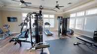 This dedicated fitness center is thoughtfully designed to support a comprehensive workout experience. The space features hardwood-style flooring paired with neutral-toned walls and elegant crown molding, giving the room a polished, upscale feel that sets it apart from a typical gym environment. Two ceiling fans are mounted overhead, ensuring consistent airflow and comfort during intense workouts.

Large windows on multiple walls flood the space with natural light, creating an open and energizing atmosphere. The equipment lineup is extensive and well-curated, including a multi-station cable and weight machine ideal for a wide range of strength training exercises, a dedicated functional trainer for cable-based movements, a treadmill for cardiovascular conditioning, and a rowing machine for full-body aerobic workouts. A rubber exercise mat is laid out on the floor, providing a designated area for stretching, floor exercises, or free-weight training.

The layout is spacious enough to allow users to move freely between stations without feeling cramped. The combination of high-quality equipment, thoughtful design details, and an abundance of natural light makes this fitness center a highly functional and inviting space for daily exercise.