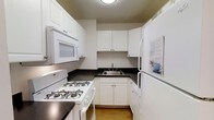 Unit 1407 is a thoughtfully designed 3-bedroom, 2-bathroom residence spread across a single level. The kitchen is efficiently laid out in a classic U-shape, featuring white cabinetry with ample storage space both above and below the counters. Dark countertops provide a clean contrast to the white cabinetry, while the stainless steel sink and white appliances — including a gas range, over-the-range microwave, and refrigerator — complete the functional cooking space. The light hardwood flooring in the kitchen adds warmth to the room. The overall design of the unit emphasizes practicality and clean lines, with a neutral color palette throughout that creates a bright and cohesive atmosphere. With three bedrooms, the unit offers flexibility for a variety of living arrangements, whether for families, roommates, or those in need of dedicated home office space. The two full bathrooms add everyday convenience. The single-floor layout ensures seamless flow between all living areas, making the space accessible and easy to navigate. This unit combines classic finishes with a sensible floor plan to deliver a comfortable and livable home environment.