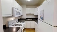 Unit 1407 is a thoughtfully designed 3-bedroom, 2-bathroom residence spread across a single level. The kitchen is efficiently laid out in a classic U-shape, featuring white cabinetry with ample storage space both above and below the counters. Dark countertops provide a clean contrast to the white cabinetry, while the stainless steel sink and white appliances — including a gas range, over-the-range microwave, and refrigerator — complete the functional cooking space. The light hardwood flooring in the kitchen adds warmth to the room. The overall design of the unit emphasizes practicality and clean lines, with a neutral color palette throughout that creates a bright and cohesive atmosphere. With three bedrooms, the unit offers flexibility for a variety of living arrangements, whether for families, roommates, or those in need of dedicated home office space. The two full bathrooms add everyday convenience. The single-floor layout ensures seamless flow between all living areas, making the space accessible and easy to navigate. This unit combines classic finishes with a sensible floor plan to deliver a comfortable and livable home environment.