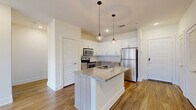 Located at 535 Main St in Nashville's 37206 zip code, this well-appointed two-bedroom, two-bathroom residence offers a thoughtfully designed single-floor layout. The open-concept kitchen and living area serves as the heart of the home, anchored by a central island with a granite countertop, undermount sink, and pendant lighting. The kitchen is fully equipped with stainless steel appliances—including a refrigerator, range, microwave, and dishwasher—complemented by white upper cabinetry, warm wood-toned lower cabinets, and a classic subway tile backsplash. Hardwood-style flooring flows throughout the main living areas, while a ceiling fan and sliding glass doors leading to a balcony bring natural light and airflow into the living space. Both bedrooms are carpeted and offer generous natural light through large windows with views of the surrounding neighborhood. Each bedroom is served by a dedicated bathroom, with one featuring a wood-toned vanity, granite countertop, and warm vanity lighting. Spacious walk-in closets with wire shelving provide ample storage. The clean, neutral color palette and modern finishes create a bright, cohesive ambiance throughout the entire residence.
