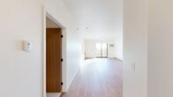 This single-floor residence offers a thoughtfully designed layout across two bedrooms and two bathrooms. The open-concept living and kitchen area is highlighted by warm hardwood-style flooring, crisp white walls, and abundant natural light streaming through a large sliding glass door that leads to a private balcony with open outdoor views. Baseboard heating and a wall-mounted AC unit ensure year-round comfort in the main living space.

The primary bedroom is a generously sized, carpet-floored retreat bathed in natural light from dual windows. It features direct access to a private en-suite bathroom equipped with a walk-in shower, wood-toned vanity with a stone-style countertop, and hardwood-style flooring. A spacious walk-in closet with wire shelving and hanging rods provides ample storage.

The second bedroom is also carpet-floored and bright, benefiting from natural light. A dedicated laundry room houses a full-size Whirlpool top-load washer and dryer set, complemented by overhead wire shelving for added utility. Two closets throughout the residence further enhance storage capacity. The clean, neutral palette and functional layout make this a highly practical and comfortable living space.