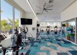 Located at 5375 NW Seventh St in Miami, FL, this well-appointed fitness center offers a bright, open, and energizing environment designed to support a full range of workout routines. The space is characterized by soaring ceilings, large floor-to-ceiling windows, and glass-paneled walls that flood the interior with abundant natural light and provide views of the surrounding palm-lined outdoor area, reinforcing the vibrant Miami atmosphere.

The main workout floor is generously sized and features a bold, geometric patterned carpet in shades of teal, blue, and gray, lending a modern and dynamic aesthetic throughout. The space is equipped with a comprehensive array of cardio machines, including treadmills and ellipticals, as well as a variety of strength training equipment and cable machines. Wall-mounted flat-screen televisions are positioned throughout for entertainment during workouts.

A dedicated glass-enclosed studio room provides a separate space for functional training and group fitness activities, stocked with exercise balls and additional accessories. Ceiling fans are distributed across the facility to maintain comfortable airflow. Mirrored walls in key areas enhance the sense of space and support form monitoring during strength training. The overall design balances functionality with a clean, contemporary aesthetic suited to an active Miami lifestyle.