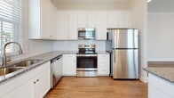 Located at 354 Fife Way in Myrtle Beach, South Carolina, this single-story home offers a clean, modern design with a cohesive aesthetic throughout. The interior is defined by warm hardwood-style flooring that extends through the main living areas and hallways, complemented by crisp white walls, crown molding, and recessed lighting.

A welcoming entry hallway leads into the expansive main living area, where multiple windows allow natural light to fill the space. French doors open to the outdoors, and a ceiling fan adds both function and character. The open layout creates a seamless flow between the living area and the rest of the home.

The kitchen is well-appointed with white shaker-style cabinetry extending to the ceiling, granite countertops, a subway tile backsplash, and a full suite of stainless steel appliances including a refrigerator, range, microwave, and dishwasher. A central island with matching granite provides additional workspace and casual seating.

The bathrooms maintain a consistent design language, featuring white vanities with granite countertops and tile flooring. One bathroom includes a walk-in glass-door shower, while another offers a shower-tub combination. Additional rooms provide flexible living space with recessed lighting and crown molding details throughout.