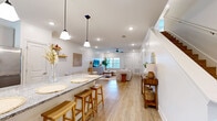 Located at 945 Schillinger Rd S in Mobile, Alabama, this two-story home offers three bedrooms, two bathrooms, and a thoughtfully designed layout spread across two floors. The main floor hosts the majority of the living space, featuring an open-concept living room and kitchen area. The living room is bright and welcoming, with recessed lighting, crown molding, a ceiling fan, and light wood-look flooring that carries throughout the home. Large windows allow natural light to fill the space. The kitchen is well-appointed with white shaker-style cabinetry, granite countertops, stainless steel appliances including a gas range with a wall-mounted hood, a center island with bar seating, and a dedicated dining nook with open shelving. Both bathrooms echo the home's clean aesthetic, featuring granite-topped vanities, wood-look tile flooring, and a combination of walk-in glass shower and soaking tub options. The upper floor contains the bedrooms, including a spacious primary bedroom and additional bedrooms filled with natural light from wide windows offering neighborhood views. An attached garage with an automatic door provides convenient parking and storage. The home's consistent use of neutral tones, warm wood flooring, and modern finishes creates a cohesive, move-in-ready atmosphere throughout.