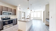 This thoughtfully designed 2-bedroom, 2-bathroom residence offers a functional and modern living experience across a single floor. The open-concept layout connects the kitchen and living room seamlessly, creating an inviting and airy atmosphere. The kitchen is a standout feature, anchored by a granite-topped island with a built-in sink and stylish pendant lighting overhead. Dark espresso cabinetry contrasts beautifully with the light granite countertops, while stainless steel appliances — including a refrigerator, range, and microwave — complete the space. Light wood-style flooring flows throughout the main living areas, enhancing the bright, clean aesthetic. The living room benefits from large windows that flood the space with natural light, complemented by a ceiling fan. Both bedrooms are carpeted and well-lit with multiple windows. The primary bedroom connects to an en-suite bathroom featuring a granite vanity, sleek cabinetry, a glass-enclosed walk-in shower with tile surround, and a spacious walk-in closet with built-in shelving and dual hanging rods. The second bathroom mirrors the same refined finishes. A hallway and two closets provide additional storage, rounding out this efficiently designed and move-in-ready home.