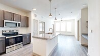 This thoughtfully designed 2-bedroom, 2-bathroom residence offers a functional and modern living experience across a single floor. The open-concept layout connects the kitchen and living room seamlessly, creating an inviting and airy atmosphere. The kitchen is a standout feature, anchored by a granite-topped island with a built-in sink and stylish pendant lighting overhead. Dark espresso cabinetry contrasts beautifully with the light granite countertops, while stainless steel appliances — including a refrigerator, range, and microwave — complete the space. Light wood-style flooring flows throughout the main living areas, enhancing the bright, clean aesthetic. The living room benefits from large windows that flood the space with natural light, complemented by a ceiling fan. Both bedrooms are carpeted and well-lit with multiple windows. The primary bedroom connects to an en-suite bathroom featuring a granite vanity, sleek cabinetry, a glass-enclosed walk-in shower with tile surround, and a spacious walk-in closet with built-in shelving and dual hanging rods. The second bathroom mirrors the same refined finishes. A hallway and two closets provide additional storage, rounding out this efficiently designed and move-in-ready home.