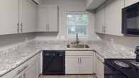 Located on Central Avenue in Charlotte's vibrant 28205 corridor, this single-floor home offers a thoughtfully updated interior with a cohesive, modern aesthetic throughout. The neutral gray color palette and clean white trim create a bright, fresh atmosphere across all living spaces.

The kitchen is a functional highlight, featuring granite countertops with a subtle white-and-gray pattern, shaker-style gray cabinetry with brushed nickel hardware, a stainless steel undermount sink, and black appliances including a dishwasher and range. A window above the sink allows natural light to filter in, offering views of the surrounding greenery.

The living and common areas are finished with durable hardwood-style flooring, lending a clean, contemporary look. Multiple bedrooms are carpeted for comfort, each receiving natural light through windows with blinds that frame outdoor views of mature trees. One larger room features dual closets with six-panel doors and hardwood-style flooring, offering flexible use as a primary bedroom or bonus space.

The bathroom is well-appointed with a granite-topped vanity, gray shaker cabinetry, a tub-shower combination with tile surround, and a lighted vanity mirror — all finished with brushed nickel fixtures that tie the space together cohesively.