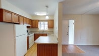 This single-floor residence offers a thoughtfully designed layout that balances functionality and comfort throughout. The kitchen is a standout feature, equipped with warm honey-toned wood cabinetry, light granite-style countertops, a double-basin sink beneath a natural light-admitting window, and white appliances including a range, dishwasher, and refrigerator. A peninsula breakfast bar provides additional counter space and creates a natural separation between the kitchen and the adjacent living area. The open living and dining area is generously proportioned, featuring neutral carpet, a ceiling fan with light fixture, textured ceiling, and sliding glass doors that lead to an outdoor balcony, filling the space with natural light. A dedicated laundry area houses a full-size washer and dryer with built-in wire shelving above for added storage convenience. The bedrooms are carpeted and well-sized, each featuring ceiling fans and windows with blinds that allow for natural light and ventilation. The two bathrooms each include a tub-shower combination — one with clean white tile surround and another with a decorative beige tile surround accented by a mosaic border strip, adding a refined touch. Warm neutral tones and consistent finishes throughout lend the space a cohesive, move-in-ready feel.