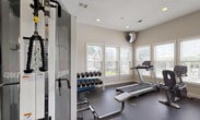 Located at 280 New Haven Blvd in Montgomery, Alabama, this single-floor fitness center is a well-equipped exercise facility designed to support a full range of workout routines. The space is organized into distinct functional zones, making it easy to navigate between cardio training, strength work, and stretching.

The cardio area lines the windowed perimeter, where multiple treadmills, an elliptical trainer, and a stationary bike are positioned facing a row of windows outfitted with adjustable blinds. These windows offer views of an outdoor pool area and surrounding greenery, providing a bright and motivating environment. A wall-mounted television is also available in this zone.

The strength training area is anchored by a Cybex multi-station cable machine, which supports a wide variety of resistance exercises. A two-tier dumbbell rack holds an organized selection of free weights, and a flat weight bench provides additional versatility. Step platforms and exercise mats are available for floor-based and functional training.

A full-length mirror spans an entire wall, visually expanding the space and allowing users to monitor their form during workouts. Recessed lighting throughout the ceiling ensures consistent illumination, complementing the natural light from the multiple windows. Durable rubber flooring covers the entire facility, providing traction and impact absorption. The overall aesthetic is clean, neutral, and functional, maintaining a professional fitness environment.