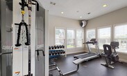 Located at 280 New Haven Blvd in Montgomery, Alabama, this single-floor fitness center is a well-equipped exercise facility designed to support a full range of workout routines. The space is organized into distinct functional zones, making it easy to navigate between cardio training, strength work, and stretching.

The cardio area lines the windowed perimeter, where multiple treadmills, an elliptical trainer, and a stationary bike are positioned facing a row of windows outfitted with adjustable blinds. These windows offer views of an outdoor pool area and surrounding greenery, providing a bright and motivating environment. A wall-mounted television is also available in this zone.

The strength training area is anchored by a Cybex multi-station cable machine, which supports a wide variety of resistance exercises. A two-tier dumbbell rack holds an organized selection of free weights, and a flat weight bench provides additional versatility. Step platforms and exercise mats are available for floor-based and functional training.

A full-length mirror spans an entire wall, visually expanding the space and allowing users to monitor their form during workouts. Recessed lighting throughout the ceiling ensures consistent illumination, complementing the natural light from the multiple windows. Durable rubber flooring covers the entire facility, providing traction and impact absorption. The overall aesthetic is clean, neutral, and functional, maintaining a professional fitness environment.
