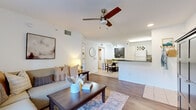 This single-floor residence offers a thoughtfully designed layout that balances comfort and functionality throughout. The living room serves as the heart of the home, featuring warm hardwood flooring, a ceiling fan with light fixture, and large sliding glass doors that fill the space with natural light and open to an outdoor area with views of surrounding greenery. A sectional sofa, patterned area rug, and framed wall art create an inviting and stylish atmosphere.

The bedroom is a serene retreat, finished with the same hardwood flooring and equipped with its own ceiling fan. Multiple windows dressed in sheer white curtains and blinds allow ample natural light while maintaining privacy. A walk-in closet and a dedicated en-suite bathroom are directly accessible from the bedroom. The bathroom features tile flooring, a vanity with granite-style countertop, and a full tub-shower combination with white tile surround. Conveniently, a stacked in-unit washer and dryer is tucked just outside the bathroom.

The dining area is finished in light tile flooring and accented by track lighting overhead, accommodating a round glass-top table with upholstered chairs. A round mirror and bold botanical artwork add character to the space. The overall palette of whites, warm neutrals, and natural wood tones creates a cohesive and welcoming ambiance throughout the home.