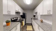 This single-floor residence offers a thoughtfully designed layout that balances functionality and modern finishes throughout. The galley-style kitchen is a standout feature, showcasing white shaker cabinetry with brushed nickel hardware, granite countertops, a white subway tile backsplash, and wood-look vinyl flooring. Black and stainless steel appliances, including an electric range, refrigerator, and dishwasher, complete the space, along with a stainless steel sink fitted beneath a classic gooseneck faucet.

The living area features rich, dark wood-look flooring and a neutral color palette, with a window that allows natural light to fill the room. A dedicated dining area connects directly to the kitchen via an open doorway, accented by a pendant light overhead, reinforcing the home's cohesive design.

Bedrooms are finished with plush carpet, neutral walls, and textured ceilings. One bedroom includes a reach-in closet with a double-door entry and built-in rod. The bathroom is equipped with a granite-topped vanity, white undermount sink, brushed nickel fixtures, a large mirror, and a tub-shower combination with white tile surround and wood-look flooring throughout.