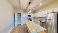 Located on Stonebench Circle in Jeffersonville, Indiana, this single-floor home offers a thoughtfully designed layout with modern finishes throughout. The kitchen serves as the heart of the home, showcasing crisp white shaker-style cabinetry, light granite countertops with subtle veining, and a generous island with a striking geometric pendant light fixture overhead. Stainless steel appliances — including a range, microwave, and dishwasher — complement the space, while a dedicated pantry provides ample storage. Light wood-look flooring runs throughout the main living areas, creating a warm and cohesive aesthetic. The bedrooms are carpeted for comfort, each featuring ceiling fans and windows that allow natural light to fill the rooms. The primary bathroom is well-appointed with rich dark wood cabinetry, dual sinks with white countertops, light wood-look flooring, and access to a spacious walk-in closet outfitted with wire shelving systems. A secondary bathroom mirrors the clean, neutral design with similar flooring and practical storage solutions. Throughout the home, neutral wall tones and clean white trim create a bright, move-in-ready atmosphere suited for a variety of interior styles.