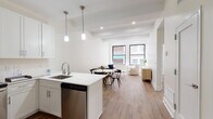 Located at 150 S Independence Mall W in Philadelphia's storied Old City neighborhood, this single-floor unit offers a clean, modern aesthetic anchored by warm wood-tone flooring and crisp white walls throughout. The open-concept living, dining, and kitchen area forms the heart of the space, where large black-framed windows flood the interior with natural light and frame views of the surrounding historic brick architecture. The kitchen is outfitted with white shaker cabinetry, quartz countertops, a peninsula with bar seating, pendant lighting, and a full suite of stainless steel appliances including a refrigerator with ice maker, range, microwave, and dishwasher. The living area offers a relaxed, airy atmosphere with exposed ceiling beams and generous room for seating arrangements. Bedrooms are well-proportioned, each featuring hardwood-style flooring, recessed lighting, and large windows that bring in city views. One bedroom includes a sliding-door closet for efficient storage. The bathroom is finished with marble-style tile flooring, white subway tile in the tub surround, a glass-enclosed soaking tub and shower, and a white vanity with a clean countertop. Recessed lighting throughout the unit ensures a bright, welcoming ambiance in every room.