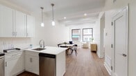 Located at 150 S Independence Mall W in Philadelphia's storied Old City neighborhood, this single-floor unit offers a clean, modern aesthetic anchored by warm wood-tone flooring and crisp white walls throughout. The open-concept living, dining, and kitchen area forms the heart of the space, where large black-framed windows flood the interior with natural light and frame views of the surrounding historic brick architecture. The kitchen is outfitted with white shaker cabinetry, quartz countertops, a peninsula with bar seating, pendant lighting, and a full suite of stainless steel appliances including a refrigerator with ice maker, range, microwave, and dishwasher. The living area offers a relaxed, airy atmosphere with exposed ceiling beams and generous room for seating arrangements. Bedrooms are well-proportioned, each featuring hardwood-style flooring, recessed lighting, and large windows that bring in city views. One bedroom includes a sliding-door closet for efficient storage. The bathroom is finished with marble-style tile flooring, white subway tile in the tub surround, a glass-enclosed soaking tub and shower, and a white vanity with a clean countertop. Recessed lighting throughout the unit ensures a bright, welcoming ambiance in every room.