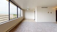 This one-bedroom, one-bathroom residence at The Heatherstone is a thoughtfully laid-out unit that makes excellent use of its space. The living area is bright and open, featuring large floor-to-ceiling windows along one wall that flood the room with natural light and frame elevated views of the surrounding cityscape and treetops. Plush carpet covers the living and bedroom areas, adding warmth underfoot, while a ceiling fan provides additional comfort. Baseboard heating runs along the windowed walls throughout.

The galley-style kitchen is efficiently designed with rich dark wood cabinetry lining both sides, providing ample storage. White appliances, including a refrigerator, dishwasher, electric range, and oven, are neatly integrated, and wood-look flooring ties the space together. The kitchen opens directly toward the unit's entryway, which features a set of bifold closet doors for added storage.

The bedroom is a comfortable, carpeted retreat with its own large window offering city views, a closet with bifold doors, and clean neutral walls that provide a versatile backdrop.

The full bathroom is clean and functional, featuring a tiled tub-shower combination, a vanity with a light stone countertop, and wood-look flooring that complements the rest of the unit's finishes.