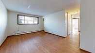 Located at 219 3rd Ave SW in Forest Lake, Minnesota, this two-bedroom, one-bathroom unit offers a practical and well-organized single-floor layout. The living room features warm hardwood-style flooring, a textured ceiling, and a window with wood-trimmed blinds that brings in natural light, along with baseboard heating for year-round comfort. Adjacent to the living area, the kitchen is equipped with rich dark wood cabinetry, granite-look countertops, a stainless steel refrigerator, and an electric range, all complemented by a ceiling fan overhead. A hallway connects the main living spaces to the private quarters and six closets, providing generous storage throughout. The primary bedroom offers carpeted flooring, a ceiling fan, and dual windows with wood-trimmed blinds, filling the room with natural light. The second bedroom also features carpet, a ceiling fan, and a large sliding-door closet. The bathroom is finished with classic white tile surrounding a full tub-shower combination and mosaic tile flooring. The unit's consistent use of warm wood tones, practical finishes, and well-distributed storage makes it a functional and comfortable living space.