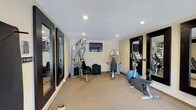 This fitness center offers a dedicated space for residents to maintain their wellness routines. The room features neutral-toned carpeted flooring and light-colored walls, creating a clean and functional environment. Recessed ceiling lighting illuminates the space evenly, complemented by a textured white ceiling. A wall-mounted flat-screen television is positioned for convenient viewing during workouts.

The facility is equipped with a multi-function cable strength training machine, a seated cable station, and a stability ball for versatile strength and core exercises. Cardio equipment includes an upright stationary bike and an elliptical trainer, providing a range of low-impact cardiovascular workout options. Large framed mirrors are positioned along the walls, enhancing the sense of space while allowing users to monitor their form during exercise.

Dark-framed glass doors provide access to the fitness center, adding a polished aesthetic detail. The overall layout is thoughtfully organized to allow comfortable movement between equipment, making it a practical and accessible amenity for daily use.