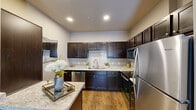 Located at 7900 McKinney Falls Pkwy in Austin, TX, this thoughtfully designed one-bedroom, one-bathroom residence offers a comfortable and modern living experience across a single floor. The open-concept kitchen and living area serves as the heart of the home, where wood-look flooring flows throughout and natural light streams in through large windows dressed with sheer curtains. A ceiling fan overhead enhances the airy feel of the living room, which provides ample space for relaxing and entertaining.

The kitchen is well-equipped and visually striking, featuring rich dark cabinetry, light granite countertops, a tile backsplash, stainless steel appliances, and a breakfast bar peninsula — ideal for casual dining or meal prep. A dedicated hallway connects the main living space to the private bedroom, which is carpeted for comfort and includes a ceiling fan, generous natural light, and access to a dedicated closet. The bedroom exudes a calm, restful ambiance with neutral tones and warm accent lighting.

The bathroom is clean and functional, offering a full tub-shower combination with large-format tile surround. A dedicated closet provides practical storage. Throughout the residence, the neutral color palette, wood-look flooring, and modern fixtures create a cohesive and inviting atmosphere well-suited for everyday living in Austin.