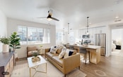 This single-floor residence offers a thoughtfully designed open-concept layout that seamlessly connects the living, dining, and kitchen areas into one cohesive, light-filled space. The living room features wood-look flooring, a ceiling fan, and large windows fitted with blinds that allow abundant natural light to fill the room. A comfortable seating arrangement anchors the space alongside a secondary sitting area with a stylish credenza and gallery wall.

The kitchen is a standout feature, showcasing a large center island with a undermount sink and bar seating, warm wood lower cabinetry paired with crisp white upper cabinets, a geometric tile backsplash, quartz countertops, and a full suite of stainless steel appliances including a range, microwave, and refrigerator. Pendant lighting above the island adds a modern touch. Adjacent to the kitchen, the dining area benefits from a large window and a black chandelier, with direct access to the outdoors via a glass-paneled door.

The bedrooms are bright and serene, carpeted for comfort, with generous windows providing natural light and views of the surrounding neighborhood. The primary bedroom includes dual windows for added brightness. The bathroom is clean and functional, featuring warm wood cabinetry, a quartz vanity top, a large mirror, and a shower-tub combination.