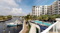 This waterfront property offers an exceptional coastal lifestyle defined by its prime location along a calm marina inlet. The exterior showcases a well-maintained multi-story building with a classic light-toned facade, generous balconies, and large windows designed to maximize the surrounding water views. Towering palm trees line the grounds, reinforcing the tropical ambiance throughout the property.

At the heart of the outdoor amenities is a resort-style swimming pool, elegantly positioned along the waterfront and surrounded by a spacious sundeck outfitted with loungers, providing an ideal setting for relaxation with open water vistas as the backdrop. The pool area is thoughtfully landscaped, blending seamlessly with the marina promenade.

The private marina runs directly alongside the property, offering boat dockage with easy access to the open waterway. A paved walkway connects the pool deck to the marina, allowing residents to move effortlessly between amenities. The combination of direct boating access, lush tropical landscaping, and panoramic water views creates a cohesive and resort-like atmosphere throughout the grounds. Whether enjoying the poolside setting or taking in the peaceful sights and sounds of the marina, this property delivers a distinctive and immersive waterfront experience.