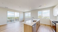 This thoughtfully designed one-bedroom, one-bathroom residence at 5280 Federal Blvd in Denver, Colorado offers a modern aesthetic with clean lines and a bright, open feel throughout. Light wood-tone flooring runs continuously across the entire space, lending warmth and visual cohesion to every room.

The combined kitchen and living area serves as the heart of the unit. The kitchen is well-appointed with white upper cabinetry, warm-toned lower cabinets, a white subway tile backsplash, stainless steel appliances including a gas range, microwave, and refrigerator, and a central island with a quartz countertop and undermount sink. Large windows and a sliding glass door with balcony access flood the living area with natural light and frame sweeping elevated views of the Denver cityscape and surrounding landscape.

The bedroom is a comfortable, well-proportioned space featuring its own sliding glass door opening to a private balcony, an additional window with panoramic views, and in-unit laundry access nearby. The bathroom is finished with a wood-toned vanity, white quartz countertop, and a tub-shower combination with marble-style tile surround. The overall ambiance is contemporary, airy, and well-lit, making efficient use of the available space.