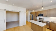 Located at 100 Medical Plaza Dr in Wylie, TX, this thoughtfully designed one-bedroom, one-bathroom residence offers a efficient and modern single-floor layout. The open-concept living, dining, and kitchen area serves as the heart of the home, anchored by a central island with granite countertops and pendant lighting overhead. The kitchen is equipped with stainless steel appliances—including a French door refrigerator, electric range, microwave, and dishwasher—complemented by warm wood-toned cabinetry, a subway tile backsplash, and light hardwood-style flooring. Natural light enters through multiple windows fitted with blinds. A stylish sliding barn door connects the main living area to the bedroom, which features neutral carpet, a ceiling fan, and a dedicated closet. The full bathroom includes a tub-shower combination with built-in shelving and a granite-topped vanity. A hallway with additional storage and a closet leads to the utility and laundry areas. The clean, neutral palette throughout—white walls, light flooring, and contemporary hardware—creates a bright and cohesive living environment well-suited for practical, modern living.