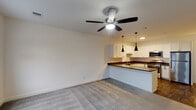 Located at Graymore Flats in Bay Shore, NY, this single-floor residence offers a clean, modern layout designed for comfortable living. The open-concept living and kitchen area forms the heart of the unit, where plush wall-to-wall carpeting meets a seamlessly connected kitchen workspace. A ceiling fan overhead provides both light and airflow, enhancing the airy feel of the space.

The kitchen is well-appointed with crisp white shaker-style cabinetry, dark countertops, and a full suite of stainless steel appliances including a gas range, dishwasher, microwave, and refrigerator. A peninsula with matching dark countertops and sleek pendant lighting above defines the boundary between the kitchen and living area, offering additional prep and seating space. Dark hardwood-style flooring grounds the kitchen zone.

The bedroom is a generously sized, carpeted retreat featuring a ceiling fan, multiple windows that invite natural light and outdoor views, and a private entry door. The bathroom is finished with light tile flooring, a sliding glass-door walk-in shower with white tile surround, chrome fixtures, and a vanity with a dark countertop — all contributing to a clean, contemporary aesthetic throughout this well-designed residence.