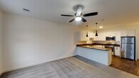 Located at Graymore Flats in Bay Shore, NY, this single-floor residence offers a clean, modern layout designed for comfortable living. The open-concept living and kitchen area forms the heart of the unit, where plush wall-to-wall carpeting meets a seamlessly connected kitchen workspace. A ceiling fan overhead provides both light and airflow, enhancing the airy feel of the space.

The kitchen is well-appointed with crisp white shaker-style cabinetry, dark countertops, and a full suite of stainless steel appliances including a gas range, dishwasher, microwave, and refrigerator. A peninsula with matching dark countertops and sleek pendant lighting above defines the boundary between the kitchen and living area, offering additional prep and seating space. Dark hardwood-style flooring grounds the kitchen zone.

The bedroom is a generously sized, carpeted retreat featuring a ceiling fan, multiple windows that invite natural light and outdoor views, and a private entry door. The bathroom is finished with light tile flooring, a sliding glass-door walk-in shower with white tile surround, chrome fixtures, and a vanity with a dark countertop — all contributing to a clean, contemporary aesthetic throughout this well-designed residence.