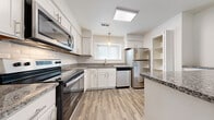 This single-floor residence in Farmington Hills, Michigan, offers a thoughtfully designed layout comprising one bedroom, a den, and one full bathroom. The living area is generously proportioned, featuring neutral-toned carpeting, soft gray walls, and a ceiling fan overhead. A sliding glass door with vertical blinds opens to an outdoor view of lush greenery, allowing natural light to fill the space. A pass-through window connects the living area to the kitchen, enhancing the open feel.

The kitchen is a standout feature, showcasing white shaker-style cabinetry, granite countertops, and a classic subway tile backsplash. Stainless steel appliances include a range, over-the-range microwave, dishwasher, and refrigerator. Wood-look vinyl flooring, a skylight, and a pendant light over the sink complete the polished, modern aesthetic.

The bedroom is carpeted and well-sized, with neutral walls and direct access to the hallway. The full bathroom features a soaking tub with white tile surround, granite-topped vanity, and wood-look flooring. A dedicated laundry area accommodates a full-size washer and dryer, adding everyday convenience to this practical and comfortable home.