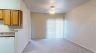 This single-floor residence offers a well-organized layout designed for everyday functionality. The living area is a comfortable, open space finished with plush carpeting and topped with a ceiling fan and light fixture. A large sliding glass door fitted with vertical blinds fills the room with natural light while providing access to the outdoors.

The galley-style kitchen is efficiently designed with warm-toned wood cabinetry lining both walls, offering ample storage above and below. White appliances, including a range, microwave, and dishwasher, are neatly integrated alongside a sink with counter space. Wood-look flooring runs throughout the kitchen, transitioning to carpet in the adjoining areas.

The bedrooms are carpeted and well-proportioned, each equipped with a ceiling fan. One bedroom features corner windows that invite natural light, while another includes access to a walk-in closet with built-in rod storage.

Both bathrooms share a consistent design, featuring wood-look flooring, a tiled tub-and-shower combination, a toilet, and a vanity with white cabinetry, a light countertop, and a wall-mounted mirror. Safety grab bars are present near the tub areas. Overall, the space maintains a neutral, light color palette that creates a clean and cohesive ambiance throughout.