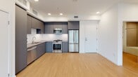 Located at 150 W Ocean Blvd in the heart of downtown Long Beach, California, this modern single-floor residence offers a well-designed open layout with contemporary finishes throughout. The main living area features light wood-style flooring, recessed lighting, and floor-to-ceiling sliding glass doors that open to a balcony, flooding the space with natural light and offering views of the surrounding cityscape, including palm trees and neighboring buildings.

The kitchen is sleek and functional, outfitted with matte gray cabinetry, a classic white subway tile backsplash, quartz-style countertops, and a full suite of stainless steel appliances including a gas range, built-in microwave, dishwasher, and French door refrigerator.

A carpeted bedroom area connects to a spacious walk-in closet featuring multiple wooden hanging rods and shelving on three walls, providing generous storage. An additional walk-in closet offers similar built-in organization.

The bathrooms are finished in a modern palette, with one featuring a walk-in shower with textured tile surround, a gray vanity with an undermount sink, and a large mirror. A second bathroom includes matching cabinetry and wood-style flooring. A carpeted hallway connects the private rooms to the main living spaces, completing this well-appointed urban residence.